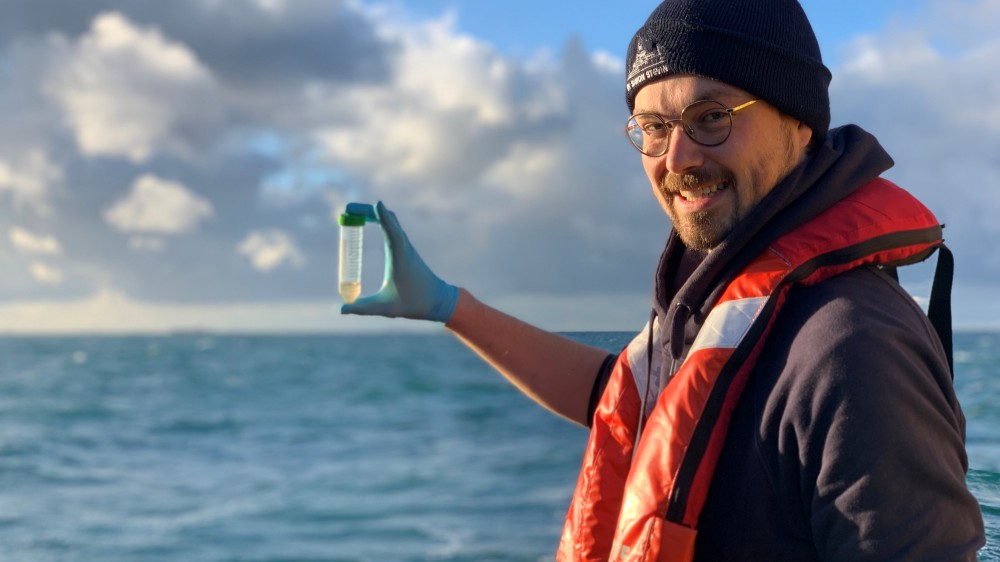 Michiel Perneel aan boord van RV Simon Stevin met een waterstaal voor metagenomics analyse