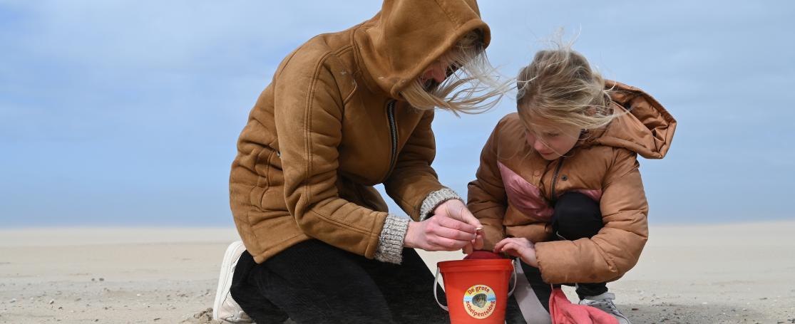 Moeder en dochten rapen schelpen op strand De Haan